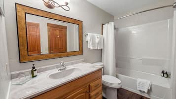 A bathroom with a large mirror, wooden vanity, white sink, toilet, and bathtub.
