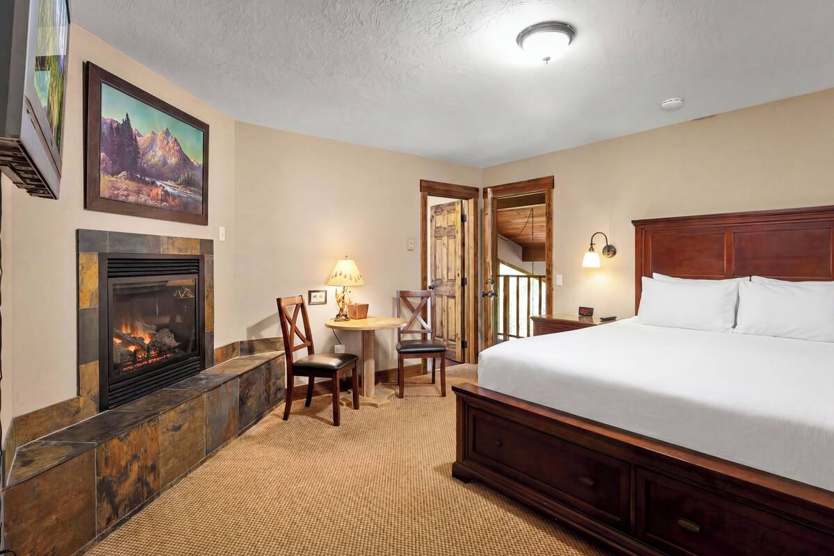 A hotel room with a fireplace, a bed, a desk with a lamp, and a staircase leading to another level.