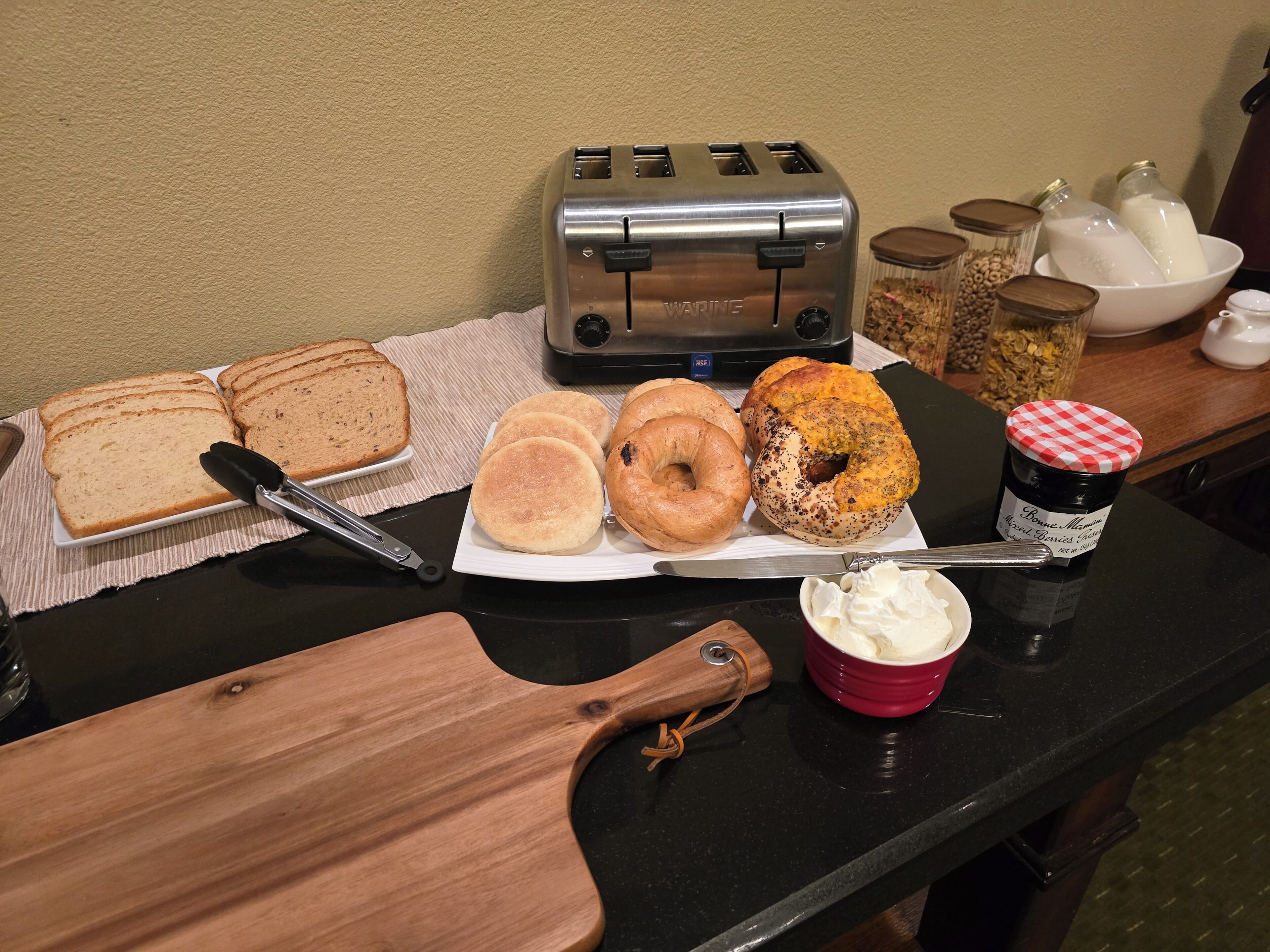A kitchen counter with a toaster, bagels, a cutting board, and a jar of butter.