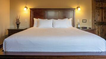 Una cama grande con sábanas blancas, cabecera de madera, lámparas de noche y una puerta de madera.