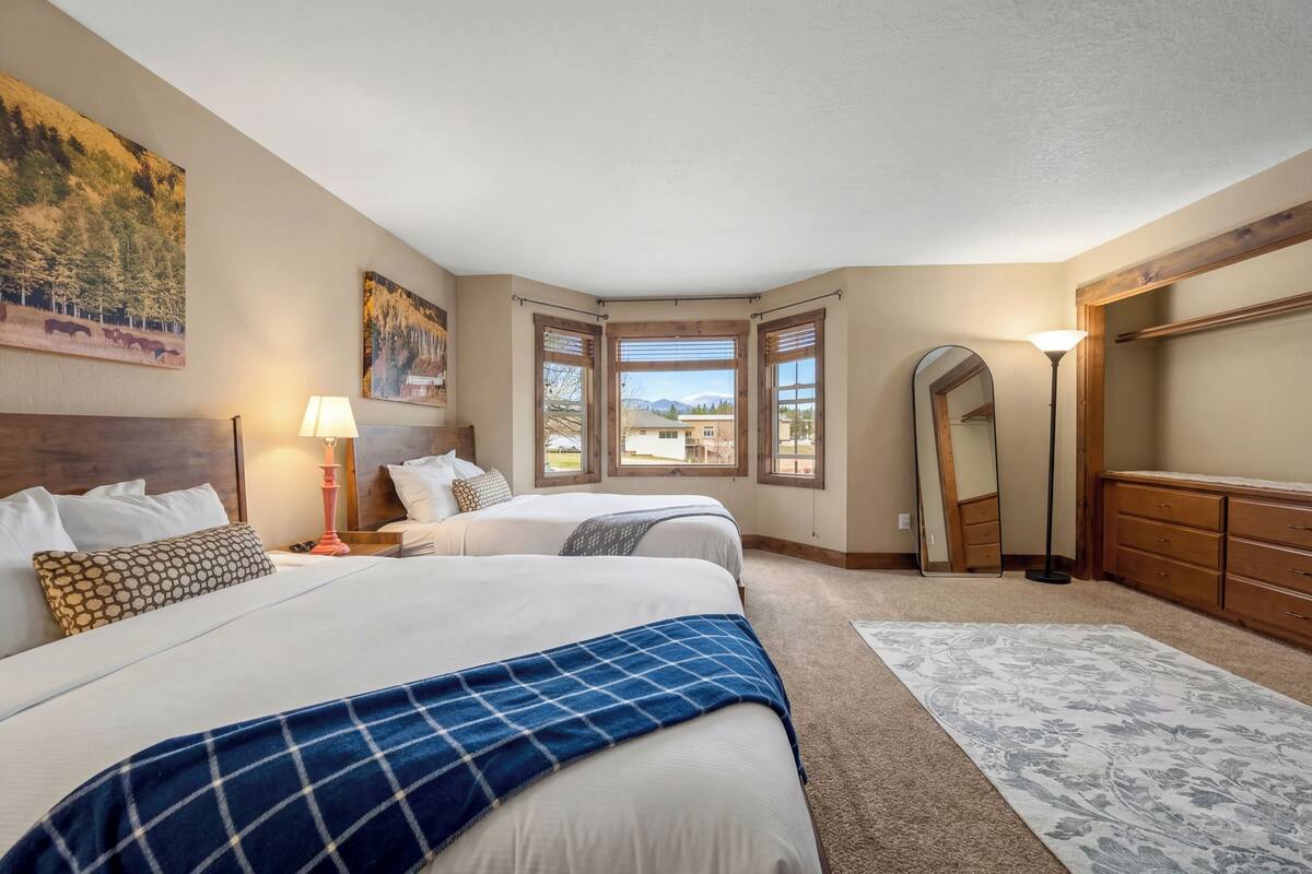 A hotel room with two beds, a large window, a mirror, and a view of the mountains.