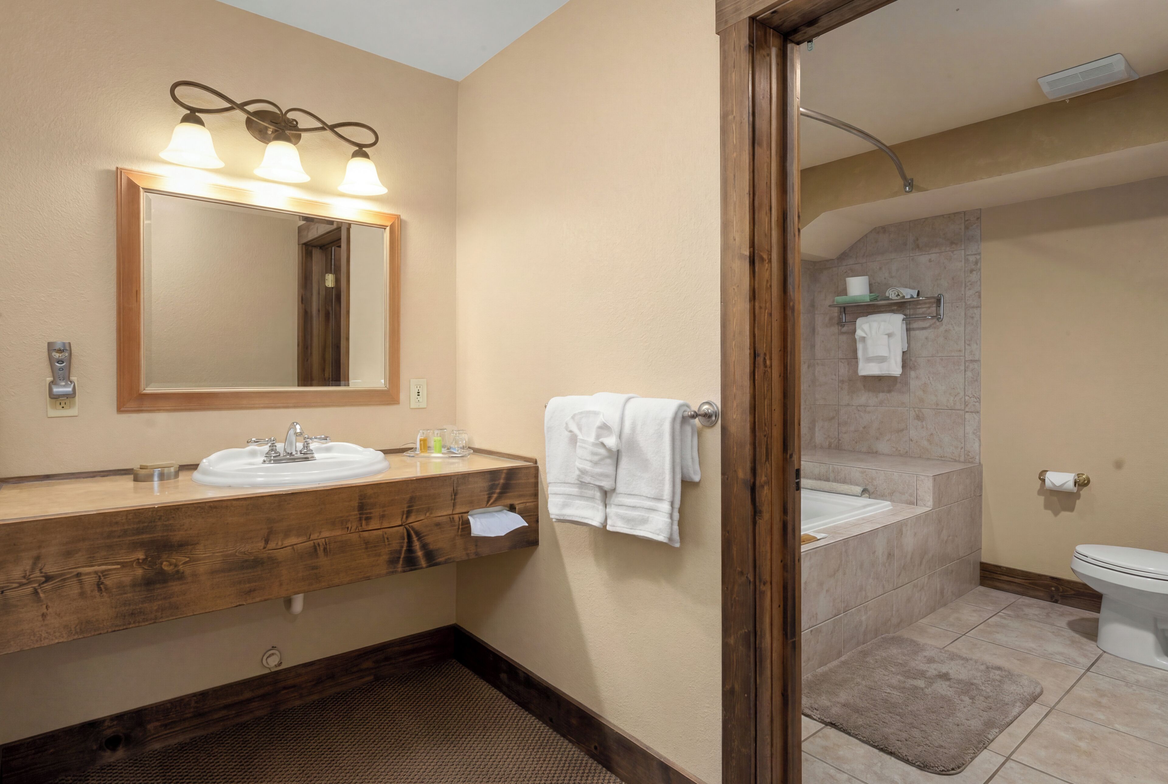 A bathroom with a wooden vanity, a mirror with lights, a bathtub, and a toilet.