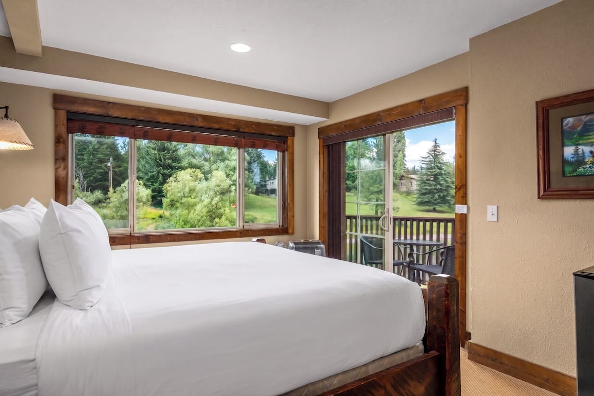 A bedroom with a large bed, two windows, a balcony, and a painting on the wall.