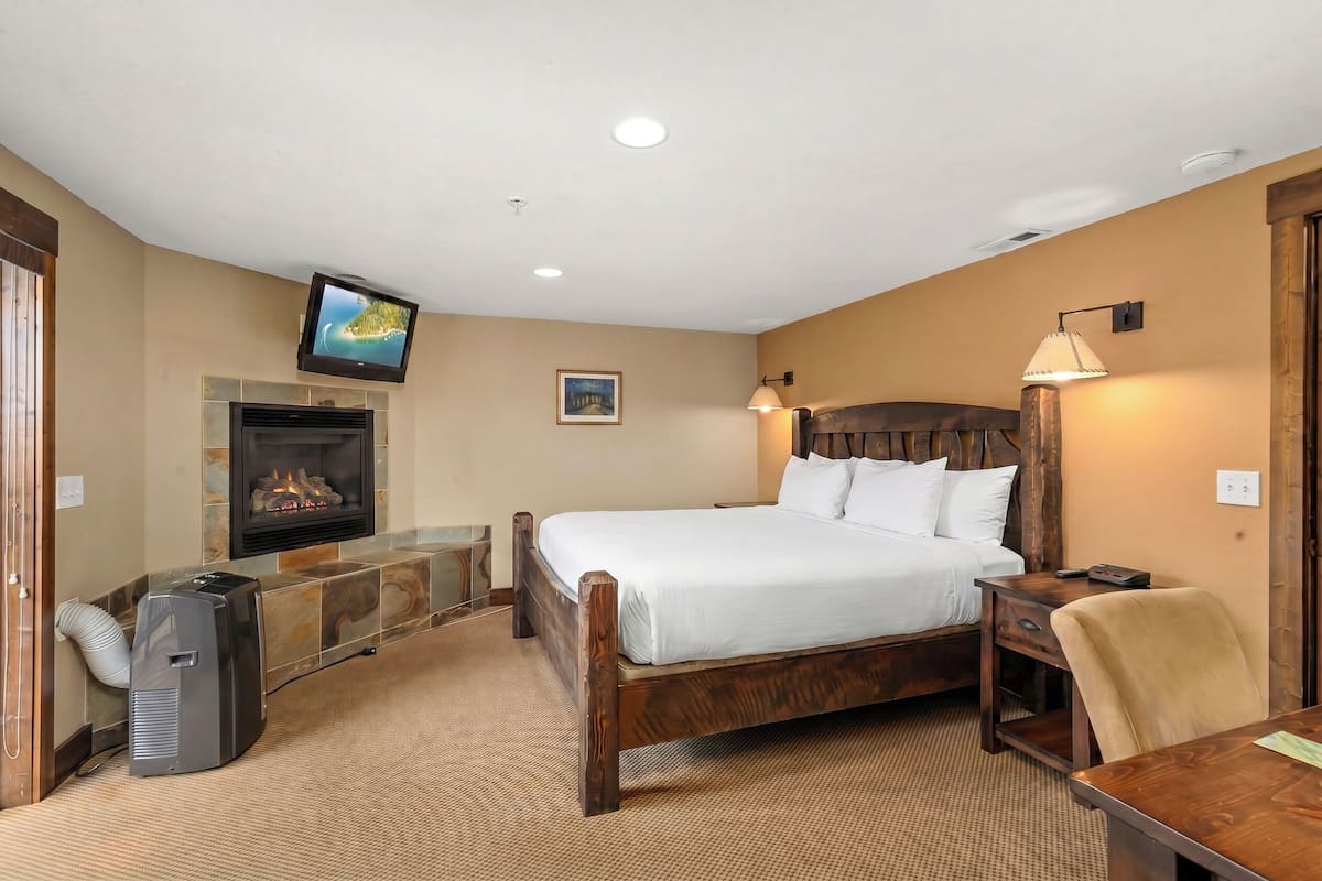 A hotel room with a bed, a TV mounted on the wall, a fireplace, a desk, and a chair.