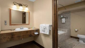 A bathroom with a wooden vanity, a large mirror with lights, a bathtub, and a toilet.