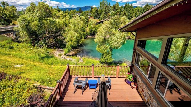 A deck with outdoor furniture overlooking a river and forested mountains. - Duck Inn Lodge (Whitefish)