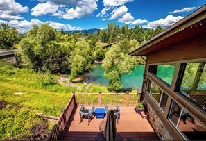 A deck with outdoor furniture overlooking a river and forested mountains. - Duck Inn Lodge (Whitefish)