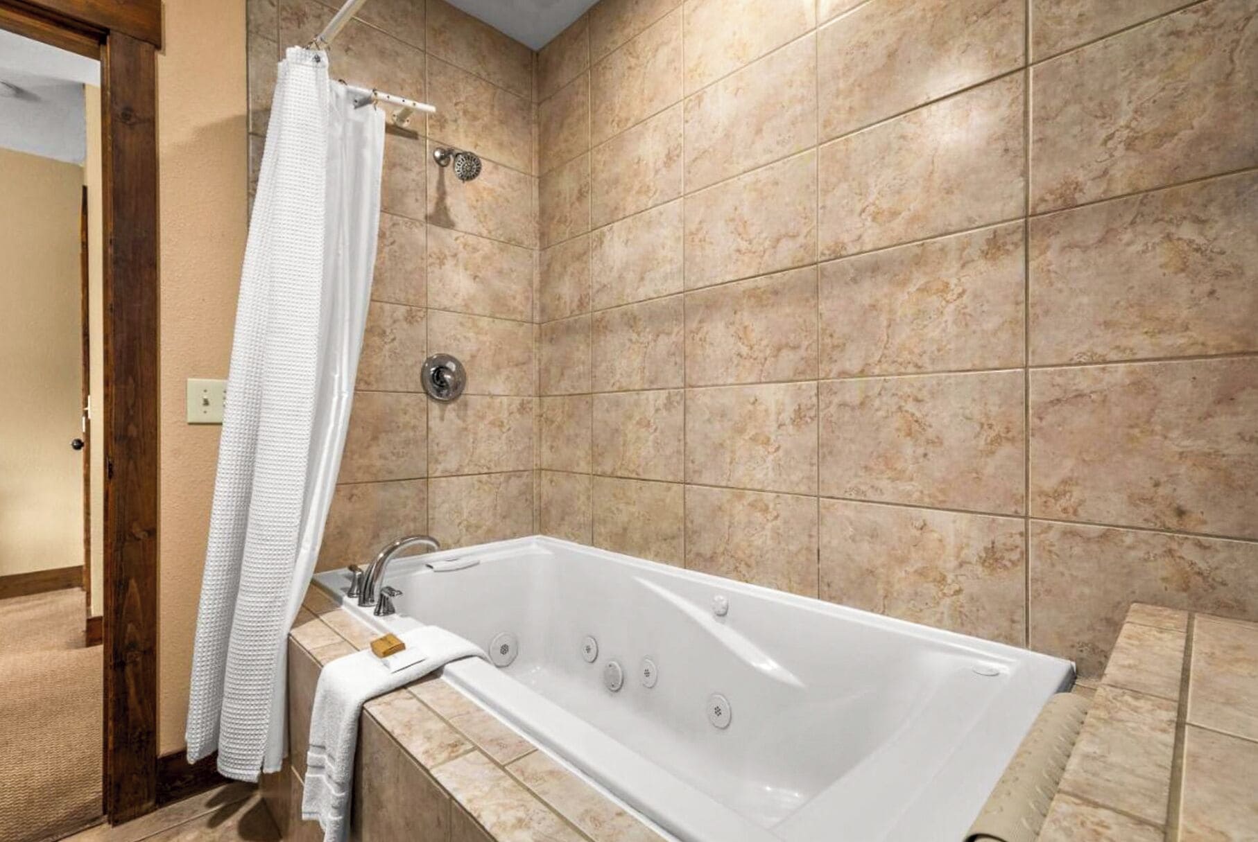 Et badeværelse med badekar, bruseforhæng og beige fliser.