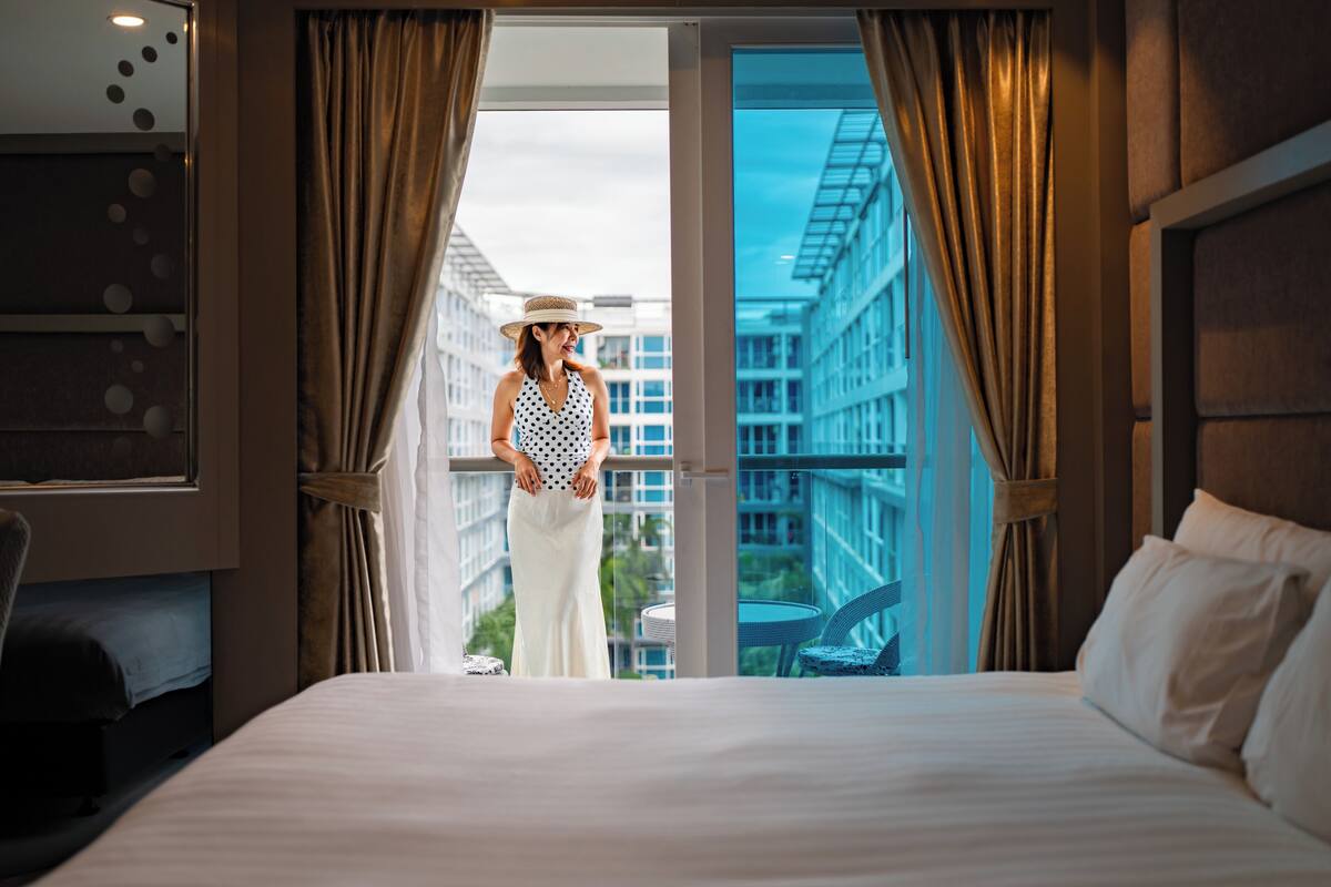 Une chambre d’hôtel avec un grand lit, une vue sur le paysage urbain à travers une porte vitrée et un balcon avec une chaise.