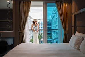 Habitación de hotel con una cama grande, vistas de la ciudad a través de un ventanal y un balcón con una silla.