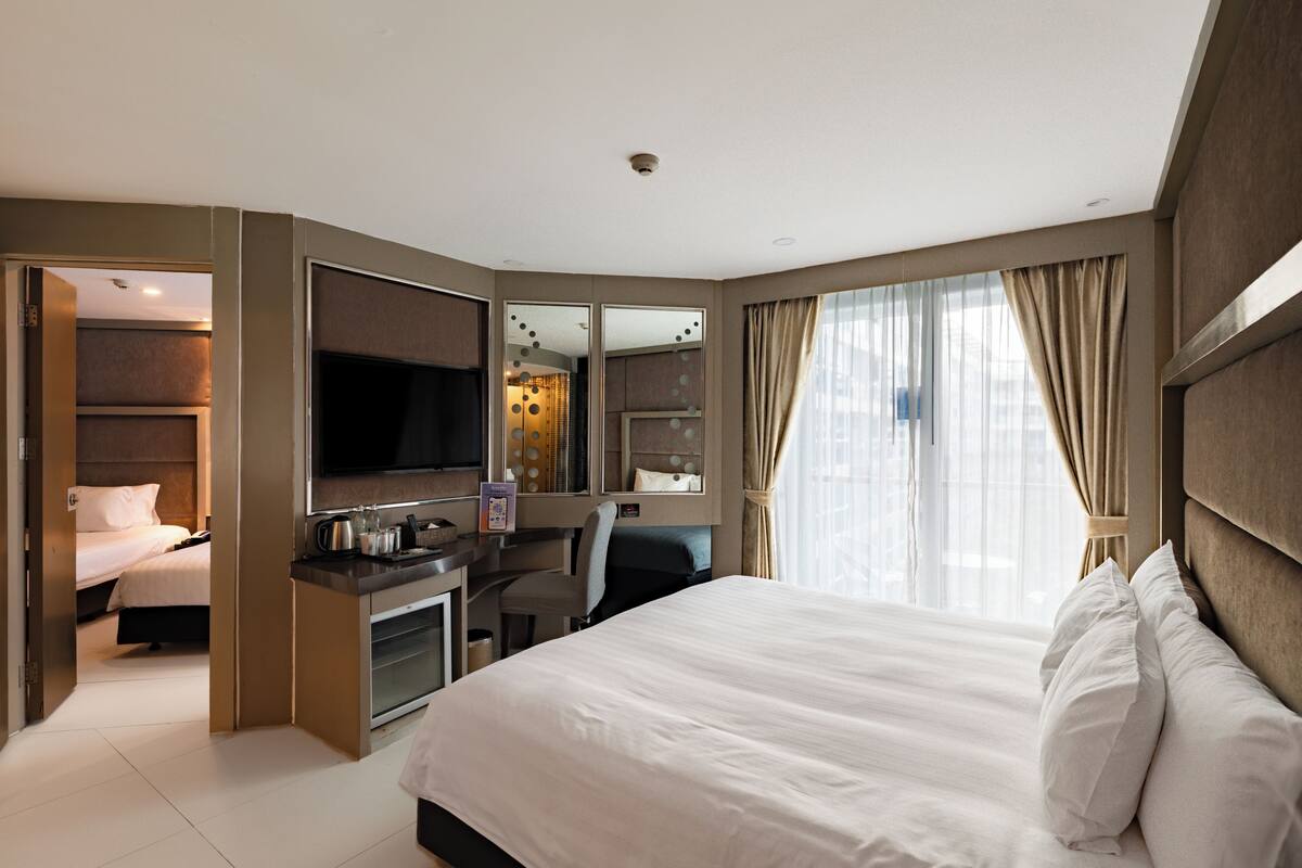 Une chambre d’hôtel moderne, dotée d’un grand lit, d’un bureau avec un ordinateur, d’une télévision et d’une salle de bain visible à travers une porte ouverte.