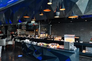 Zona de bar moderna con mostrador que exhibe diversos alimentos y un dispensador de zumos.
