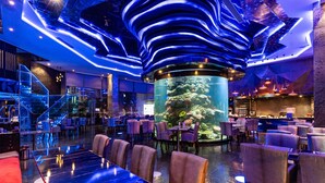 Un restaurant moderne doté d’un aquarium central, autour duquel sont disposées les tables, et d’un escalier menant à un niveau supérieur.