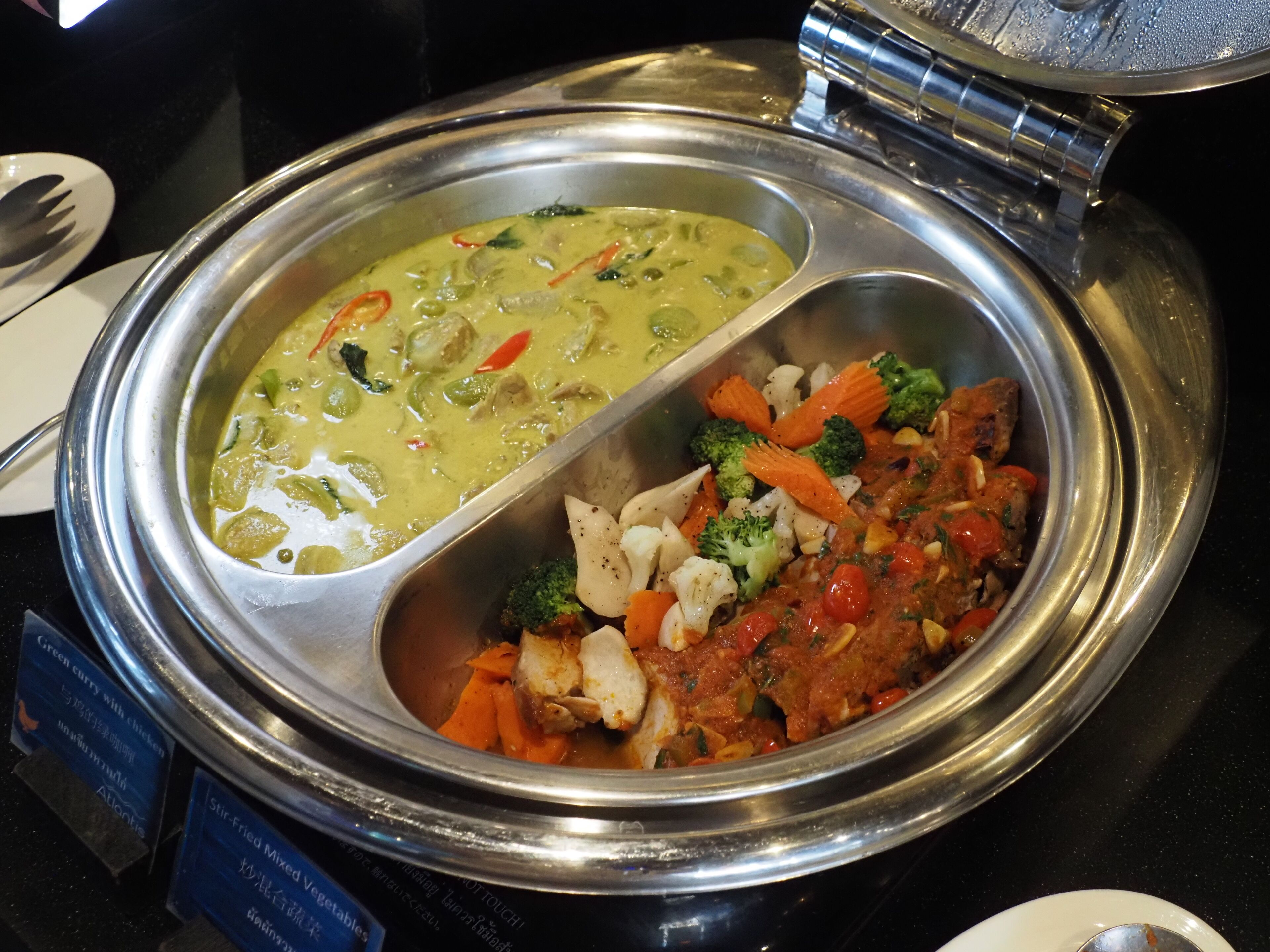 A buffet with two dishes: one appears to be a green curry with chicken and vegetables, and the other is a mixed vegetable dish with broccoli, carrots, and possibly chicken.