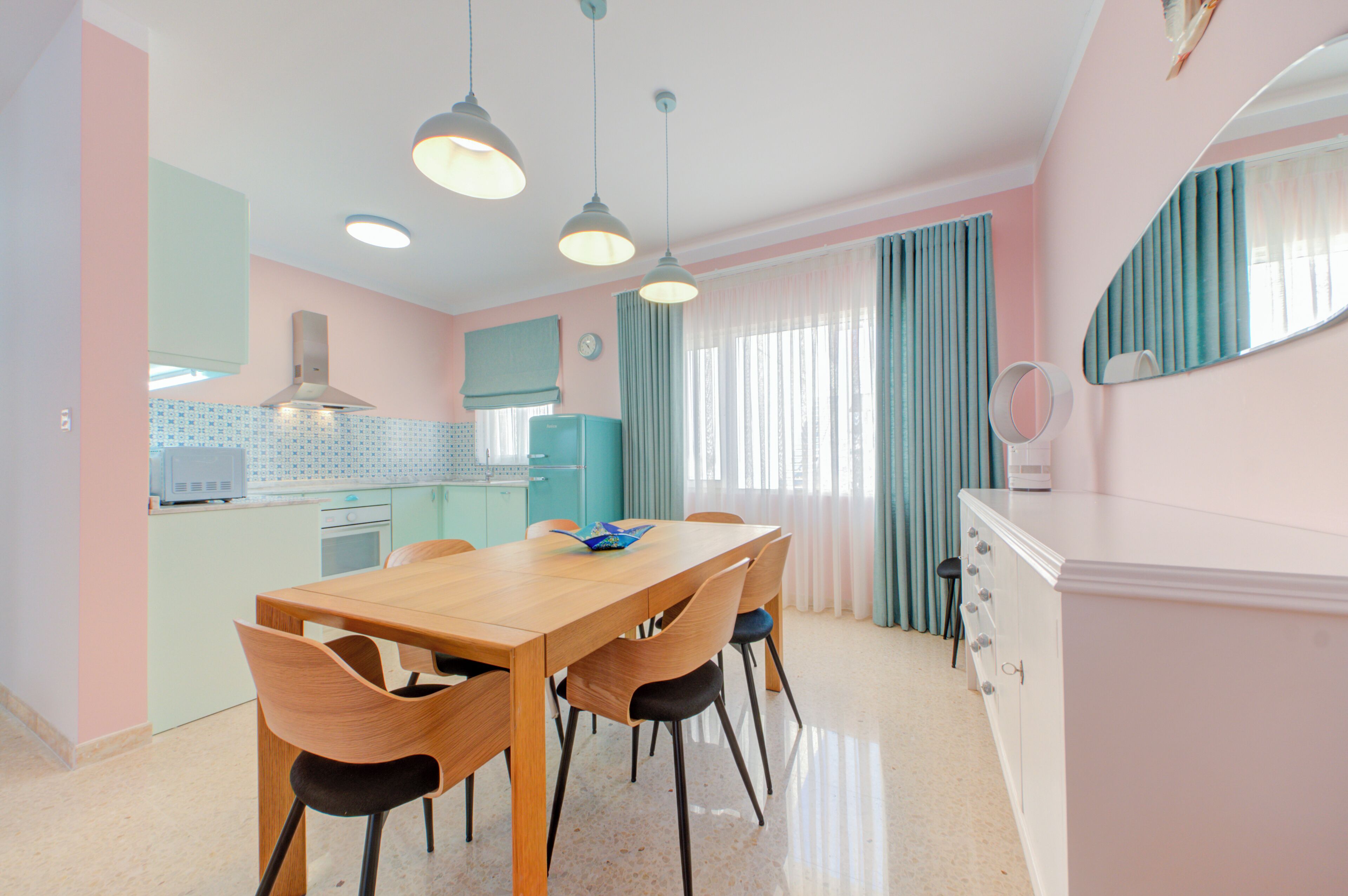 Une cuisine moderne avec une table et des chaises en bois, un four encastré et une fenêtre avec des rideaux.