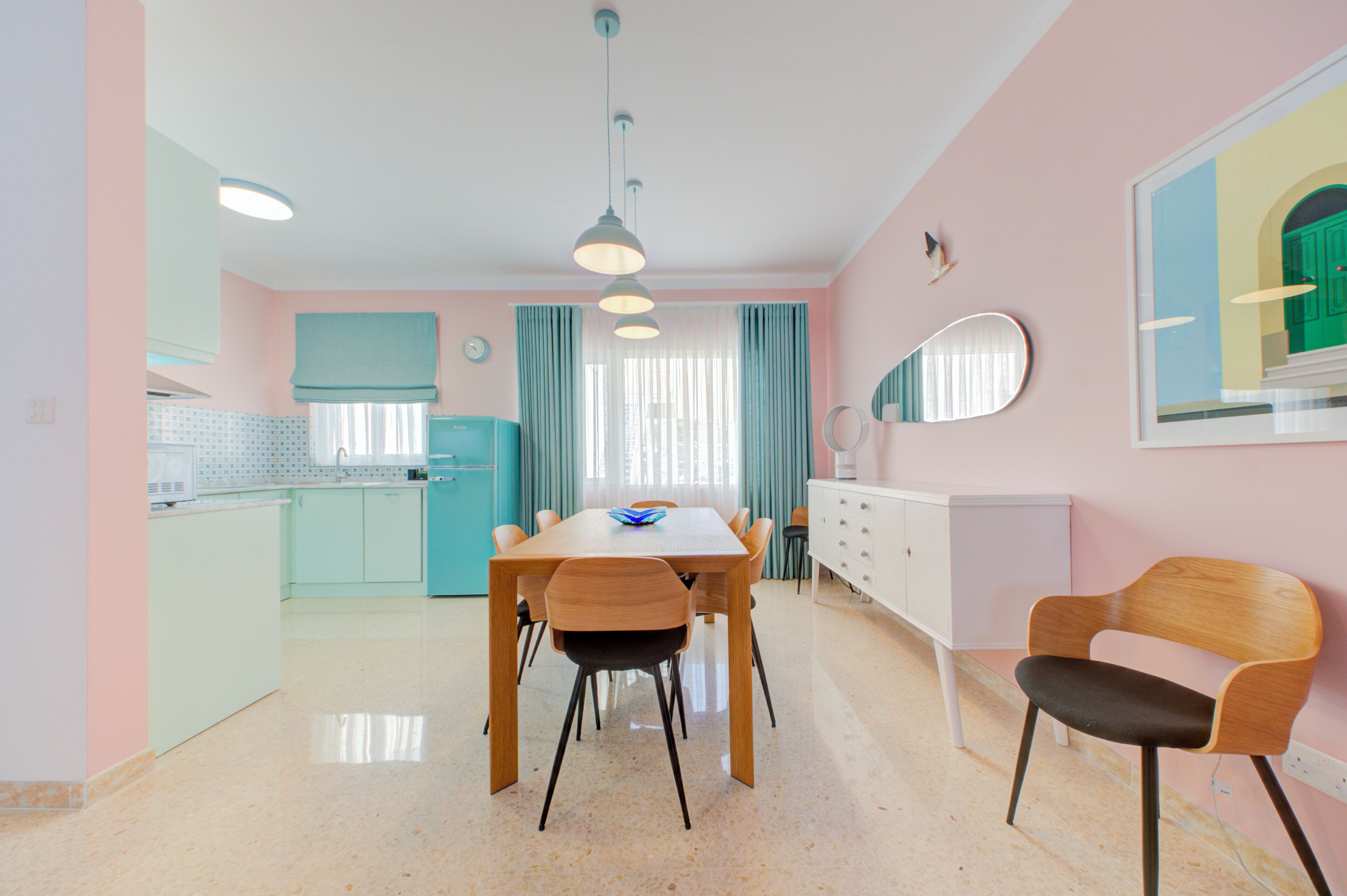 A modern kitchen with teal cabinets, a wooden dining table with chairs, and a white dresser.