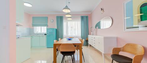 A modern kitchen with teal cabinets, a wooden dining table with chairs, and a white dresser.