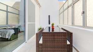 A narrow balcony with a glass table, wicker furniture, and potted plants. - Colourful Spacious Maisonette with Yard (St. Paul's Bay)