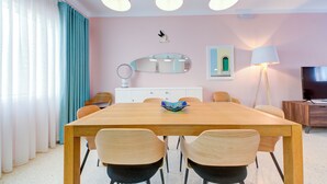 A dining area with a wooden table, four chairs, a decorative bowl, a white cabinet, a mirror, a lamp, and a television. - Colourful Spacious Maisonette with Yard (St. Paul's Bay)