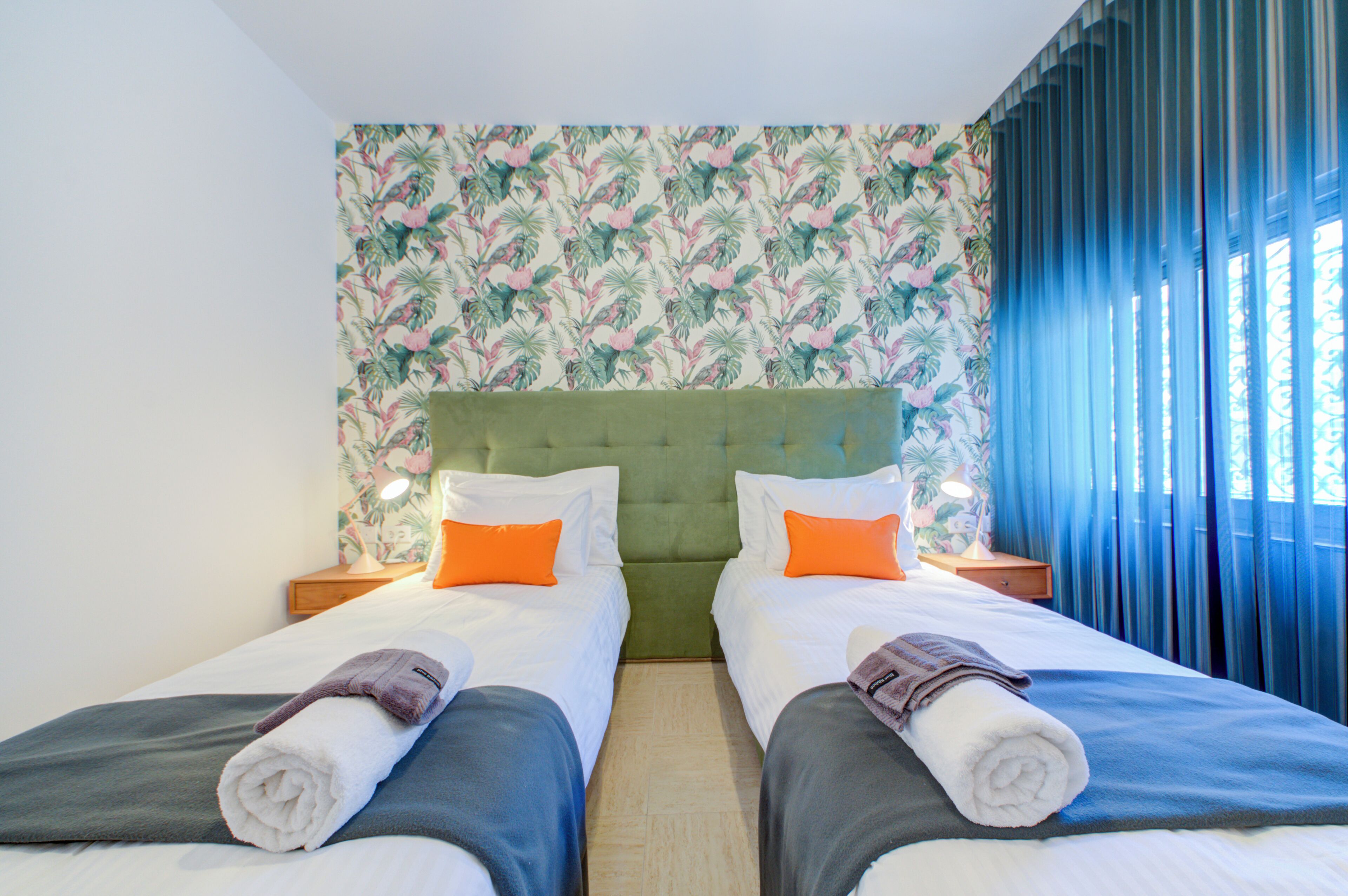 Una habitación doble con dos camas, un cabecero verde y un papel tapiz con motivos florales.