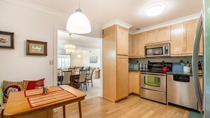 A modern kitchen with wooden cabinets, stainless steel appliances, and a dining area with a wooden table and chairs. - Spacious Condo with Stunning View (Oakland)