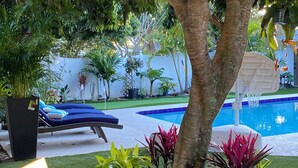 A pool area with a lounge chair, a wooden bench, and various potted plants. - Private Palm Beach Pool Home Putting Green near BEACH Restaurants (North Palm Beach)
