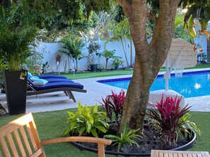 A pool area with a lounge chair, a wooden bench, and various potted plants. - Private Palm Beach Pool Home Putting Green near BEACH Restaurants (North Palm Beach)