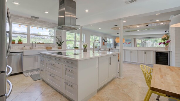 A modern kitchen with white cabinetry, a large island, and a view of greenery outside. - Private Palm Beach Pool Home Putting Green near BEACH Restaurants (North Palm Beach)