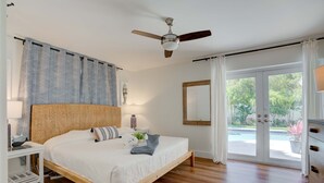A bedroom with a wooden bed, a ceiling fan, a bedside table with a lamp, and a view of a swimming pool through a glass door. - Private Palm Beach Pool Home Putting Green near BEACH Restaurants (North Palm Beach)