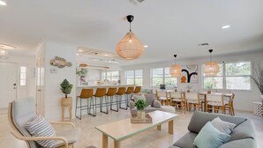 A spacious living area with a sofa, armchair, and coffee table, a dining area with chairs and a table, and a kitchen with bar stools. - Private Palm Beach Pool Home Putting Green near BEACH Restaurants (North Palm Beach)