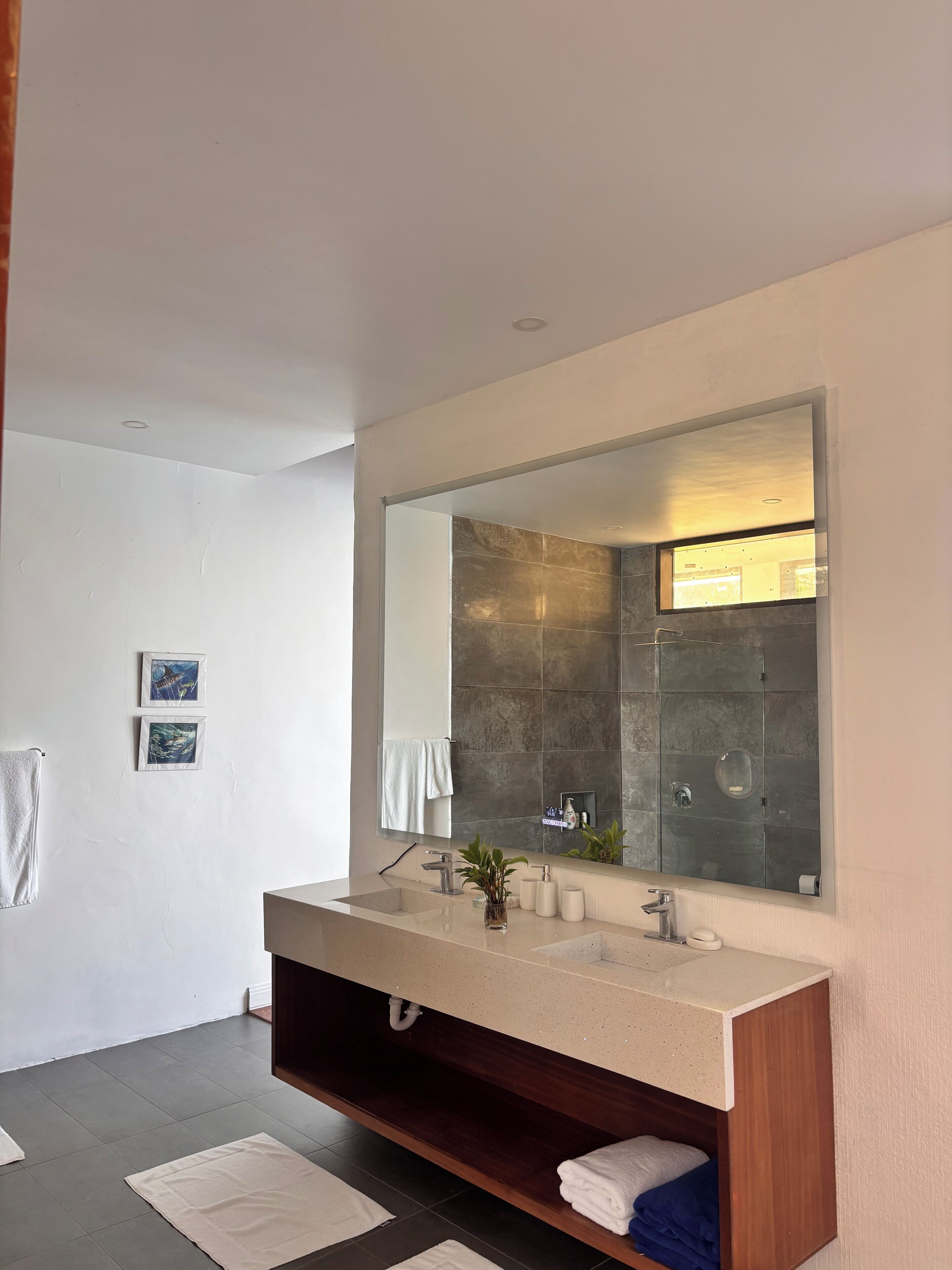 A modern bathroom with a large mirror, two sinks, a wooden vanity, and a towel rack.