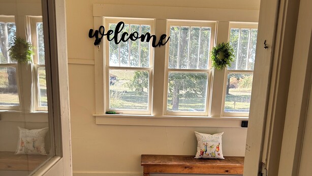 A room with a wooden bench, a welcome mat, and a window with a view of trees.
