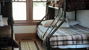 A dormitory room with bunk beds, a window with curtains, a wooden floor, and a rug.
