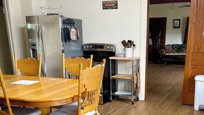 A dining area with a wooden table and chairs, a refrigerator, a stove, and a sign reading 'HUNTING CAMP RD.'