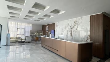 Een moderne hotellobby met een receptiebalie, een zithoek en een groot raam dat voor natuurlijk licht zorgt.