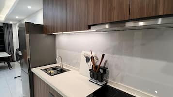 Eine moderne Küche mit dunklen Holzschränken, einem Edelstahlkühlschrank, einer schwarzen Induktionskochplatte und einer weißen Arbeitsplatte.