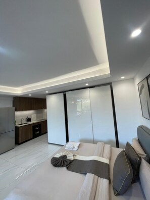 Une chambre à coucher moderne avec un grand lit, une armoire intégrée et un coin cuisine à l’arrière-plan.