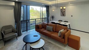A modern living room with a sofa, a small round table, and a dining area with a table and chairs. - Trendy Oasis Park Studio in Kimihurura - Kigali (Kigali)