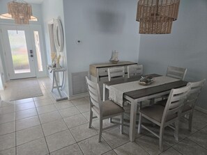 Un comedor con una mesa dispuesta para cuatro, rodeada de sillas, una mesita auxiliar y un modelo decorativo de barco.