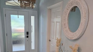 Un corridoio con una porta bianca, uno specchio, un tavolino consolle in legno con oggetti decorativi e un tappeto a motivi.