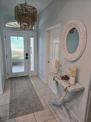 A hallway with a white door, a mirror, a wooden console table with decorative items, and a patterned rug. - Heated Pool Oasis • Pet-Friendly, Near Siesta Key (Sarasota)