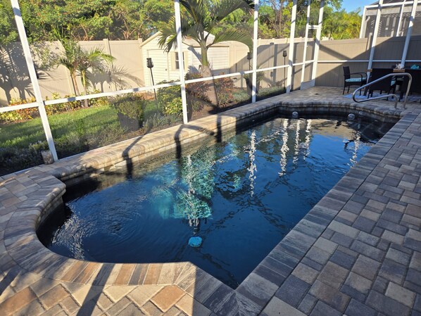 Una piscina con borde de piedra, rodeada por una valla y follaje.