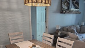 Zona pranzo con tavolo in legno, sedie bianche, lampadario intrecciato e un quadro raffigurante barche al muro.