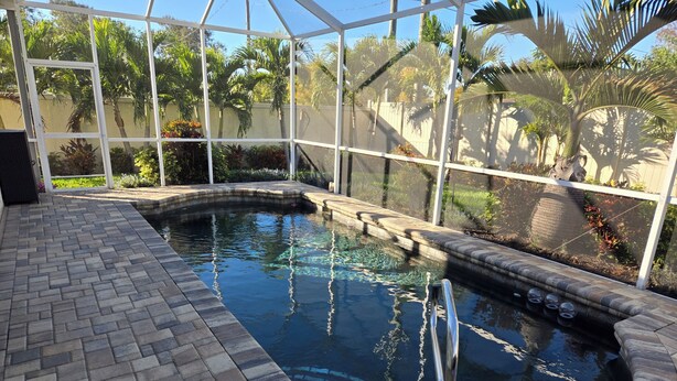 Una piscina con bordo in mattoni, circondata da un'area vetrata dove si vedono palme e piante.
