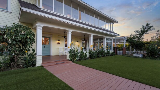 Une maison à deux étages dotée d’un porche abrité, d’une terrasse en bois rouge et d’une pelouse bien entretenue.