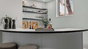 Et moderne køkken med en buet bordplade, indbyggede hylder med vinglas og et vindue med udsigt til træer.