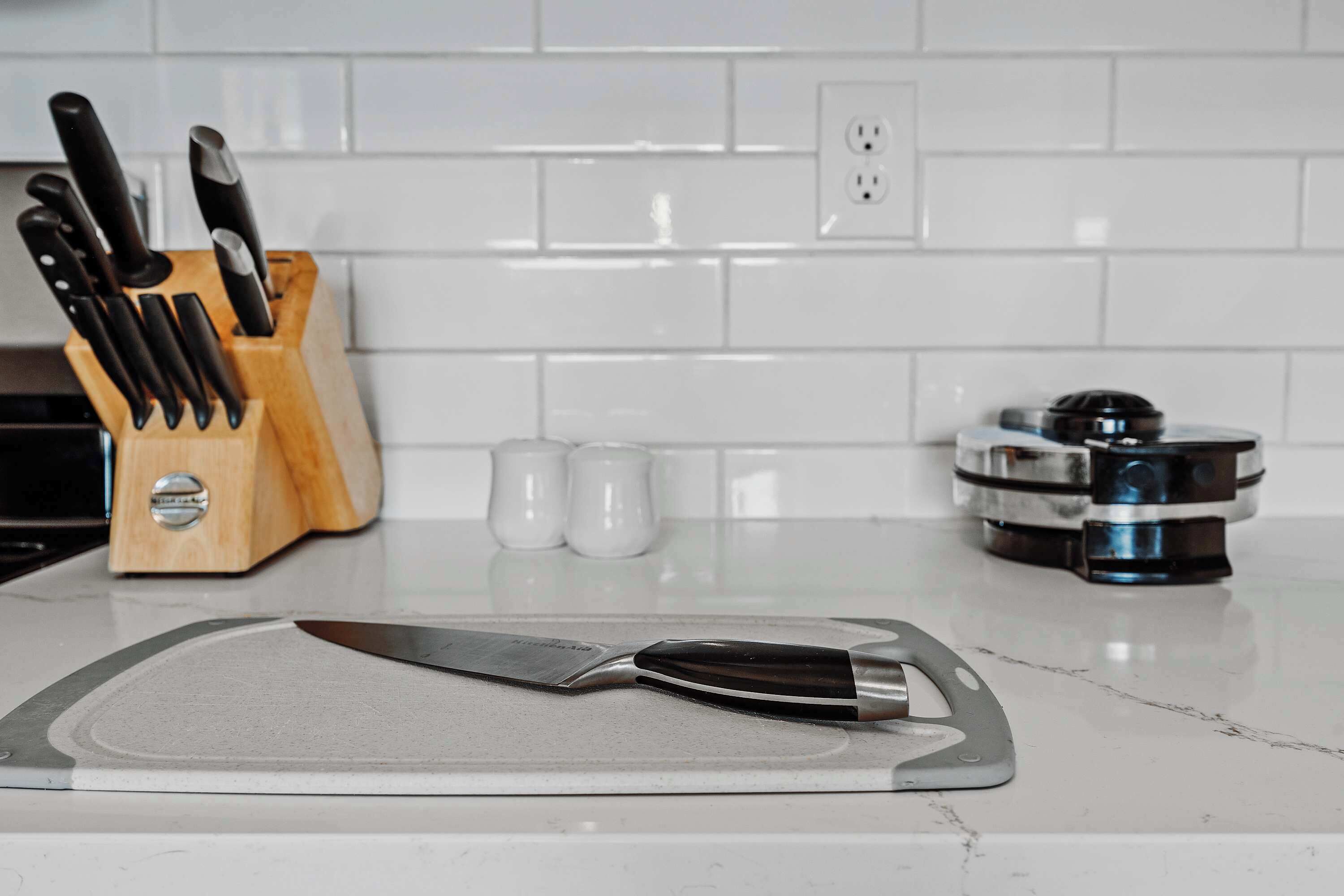 A kitchen counter with a cutting board, a knife, a knife block, salt and pepper shakers, and a coffee machine.