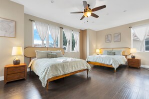 Ein Schlafzimmer mit zwei Betten, Holz-Kopfteilen, Nachttischen mit Lampen und einem Deckenventilator.