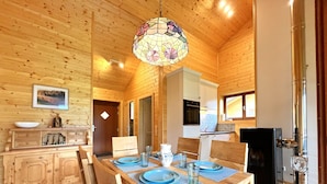 A wooden cabin interior with a dining table set for four, a kitchen area, and a wooden ceiling.