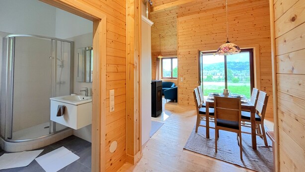 A wooden cabin interior with a shower, a dining area, and a view of the outdoors.